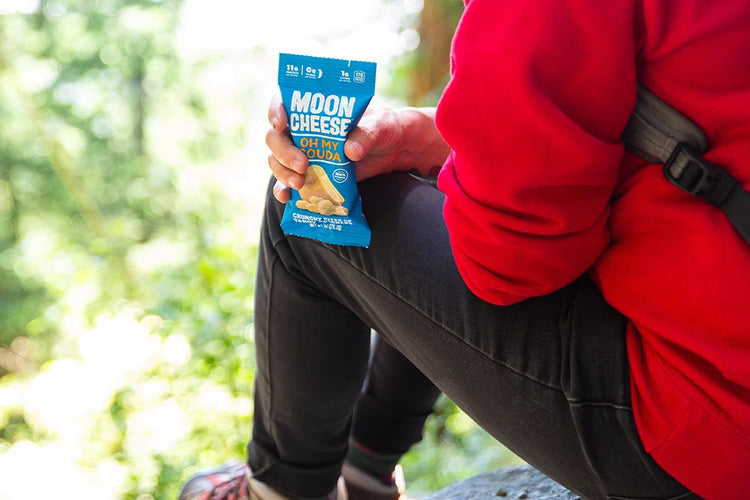 gluten free sugar free keto friendly high protein oh my gouda moon cheese in the hand of a hiker wearing a red sweatshirt on a trail. 